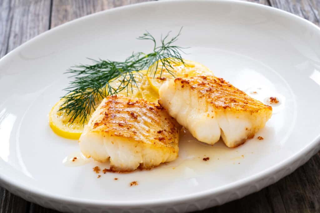 wild pacific seared cod loin fillet and sliced lemon on wood table wild pacific seared cod loin fillet and sliced lemon on wood table