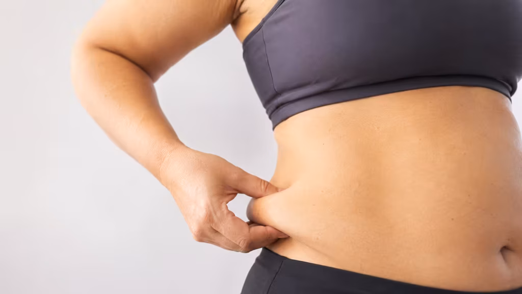 Woman gently pinching soft fat at the side of her waist.
