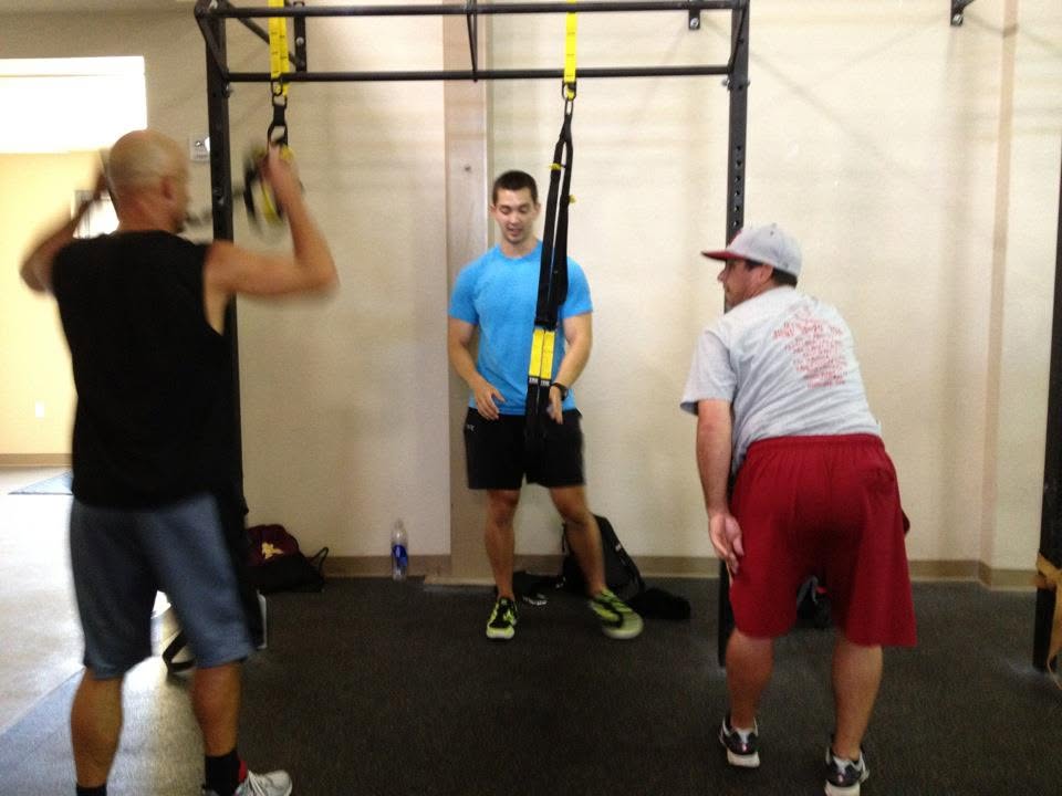Josh Schlottman supervising two clients during a gym workout with suspension straps.