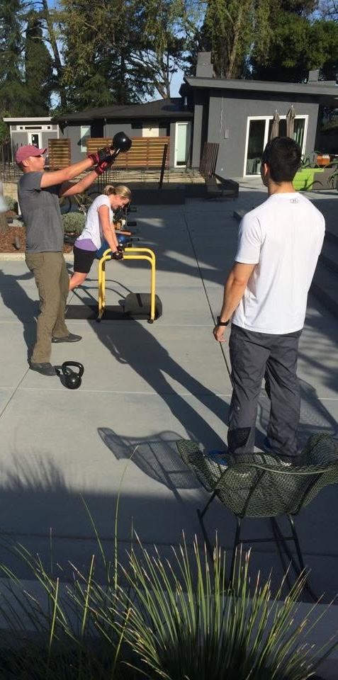 Josh Schlottman coaching two clients on a Napa Valley home patio, with one performing a kettlebell swing.