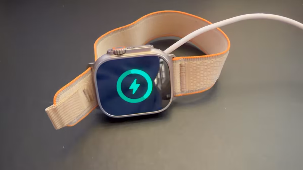 apple watch ultra 4 charging setup Apple Watch Ultra 4 charging on a dark tabletop, with a green charging indicator on the screen and a white braided cable attached.