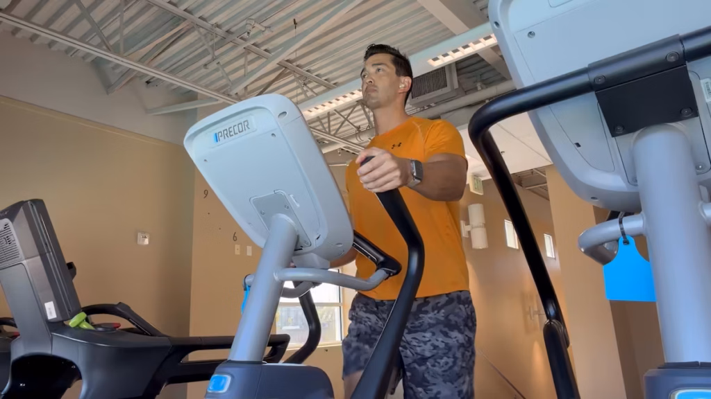 apple watch ultra 4 elliptical workout test Trainer Josh using an elliptical machine at the gym, gripping the moving handle while wearing an Apple Watch Ultra 4 on his left wrist.