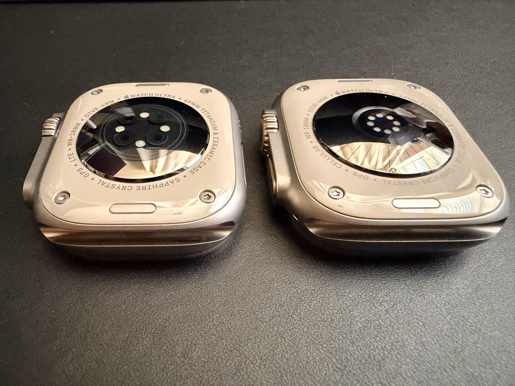 apple watch ultra4 vs ultra2 sensor layout close up Angled close-up of the backs of Ultra 2 on the left and Ultra 4 on the right; Ultra 4 has more small circular windows grouped around the center.