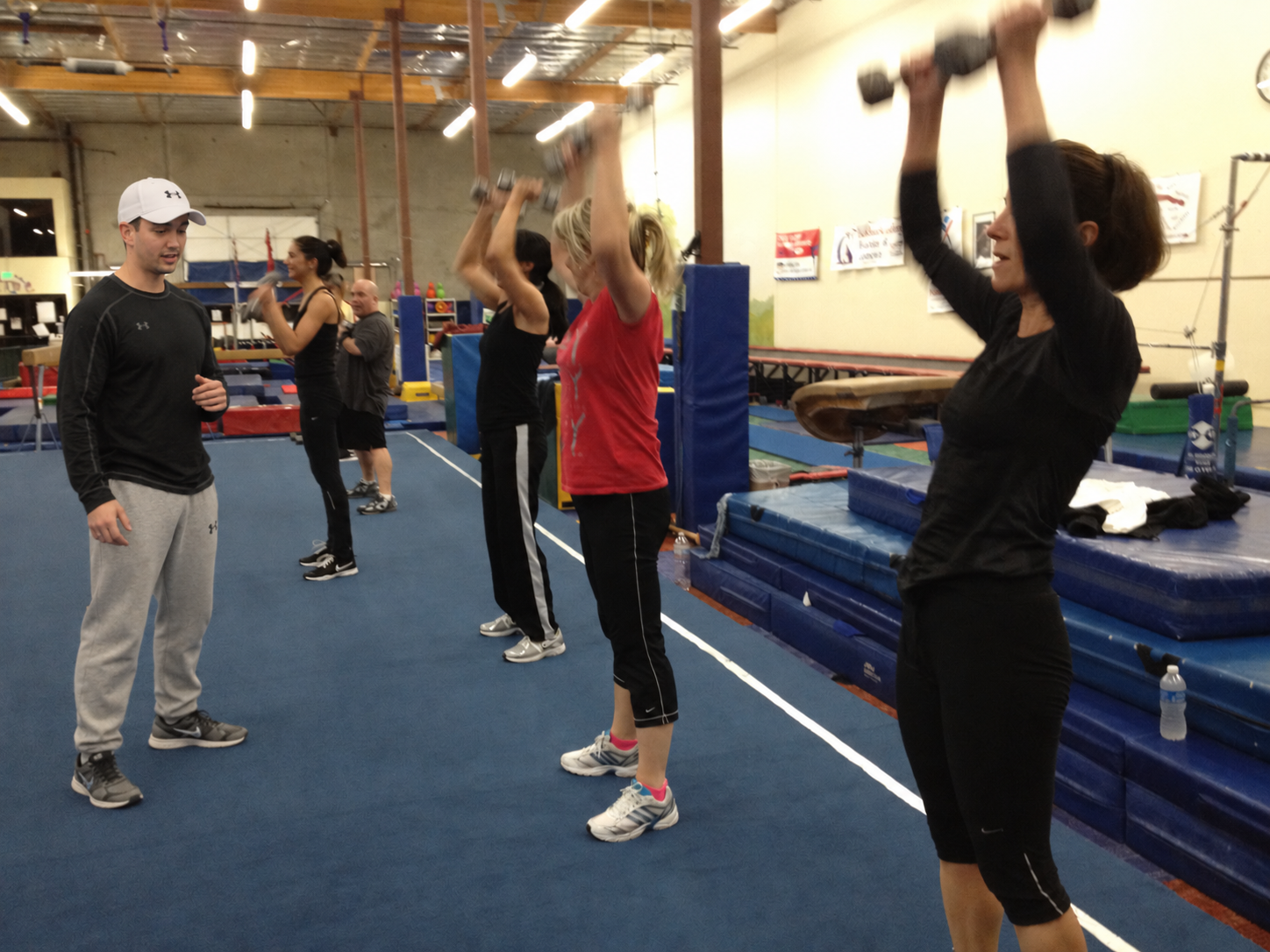 Josh Schlottman coaching a boot camp class as participants perform standing dumbbell presses in a gym.
